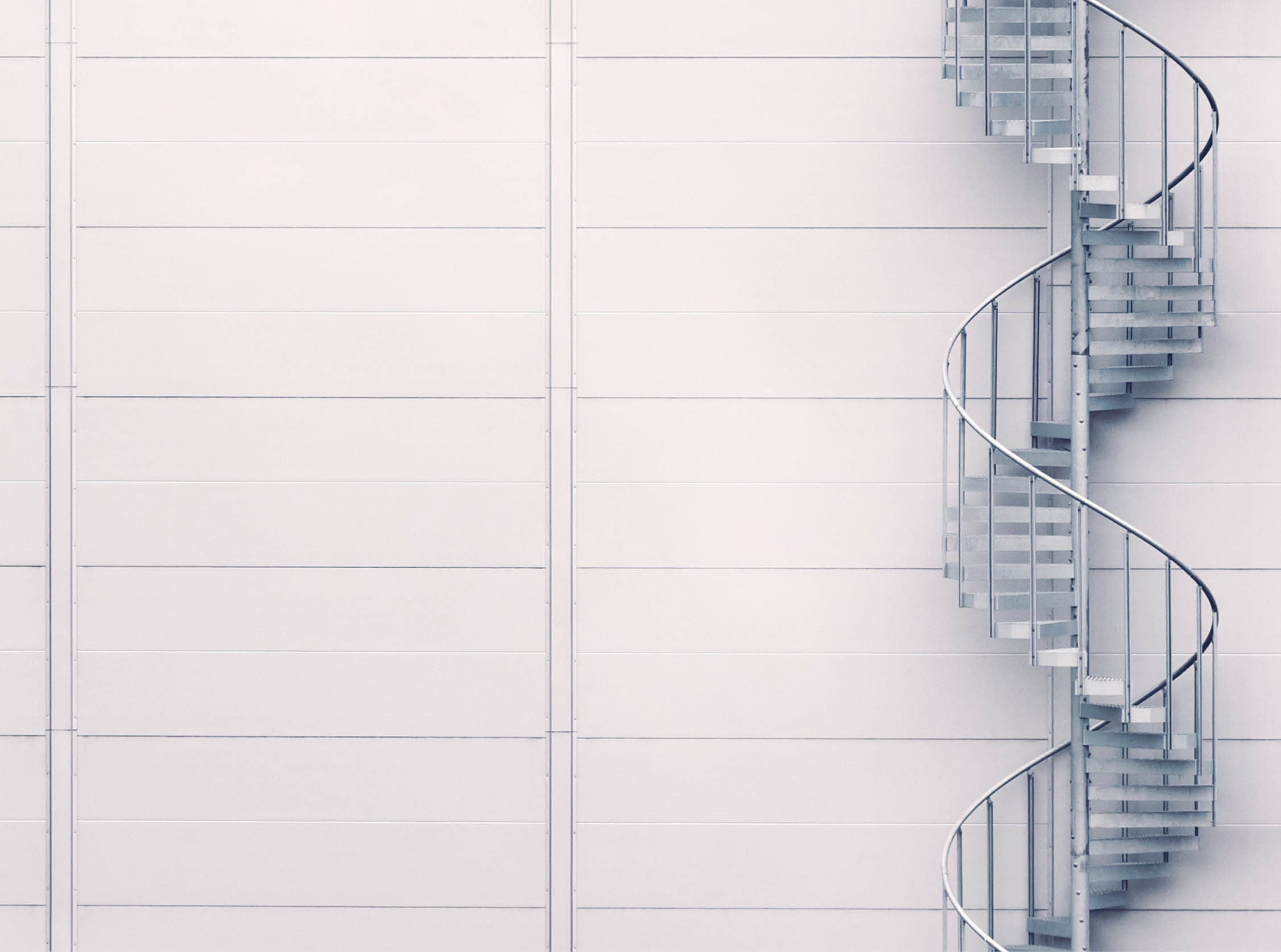 A spiral staircase leading up to a red door of an industrial building.