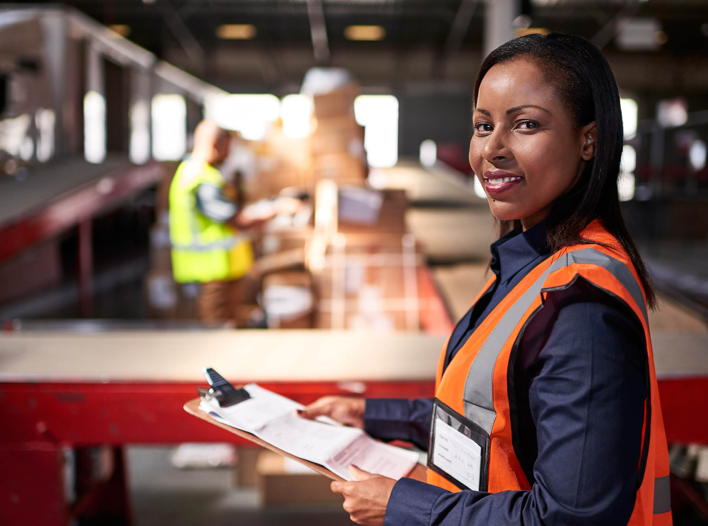 Portrait of a warehouse manager holding a clipboard with workers in the background