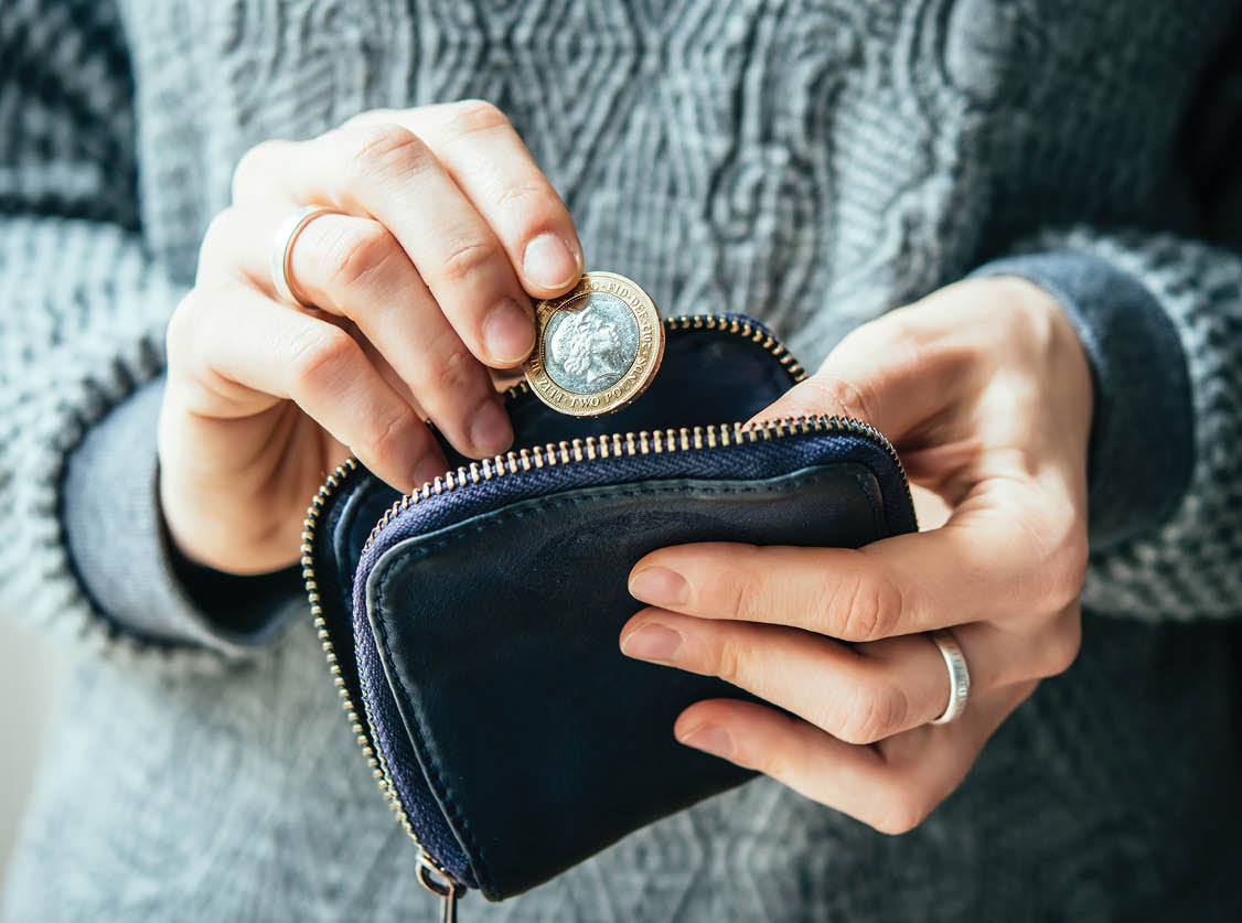 Hands holding british pound coin and small money pouch