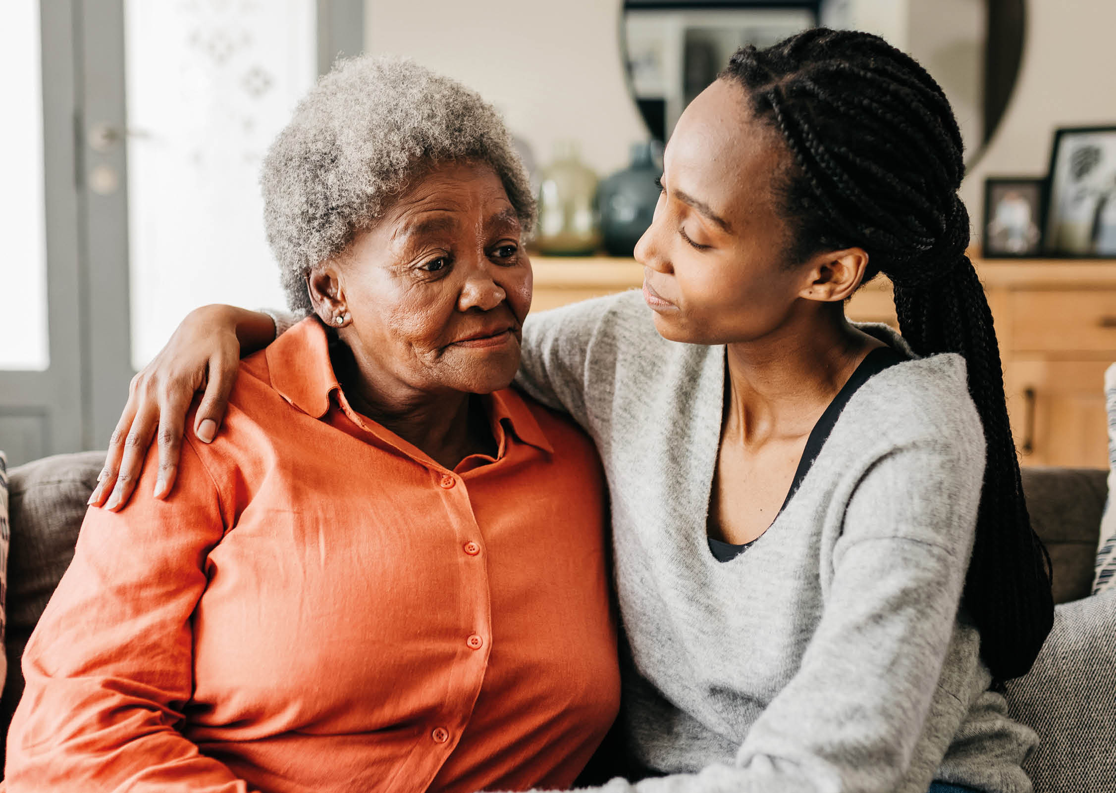 Young woman hugging sad mother comforting her on sofa at home