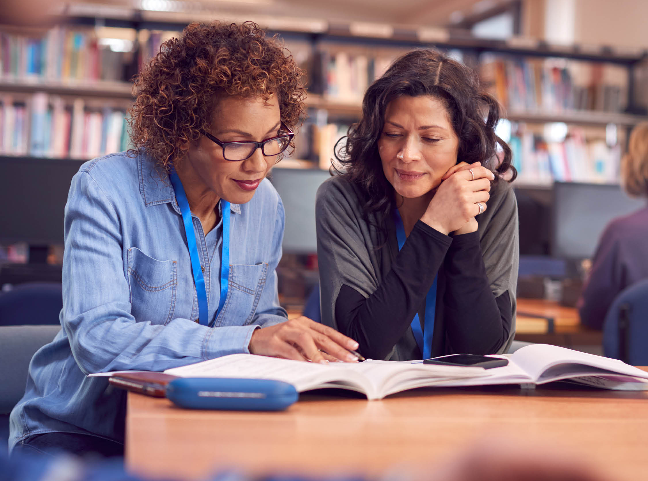 Teacher With Mature Female Adult Student Sitting At Table Working In College Library